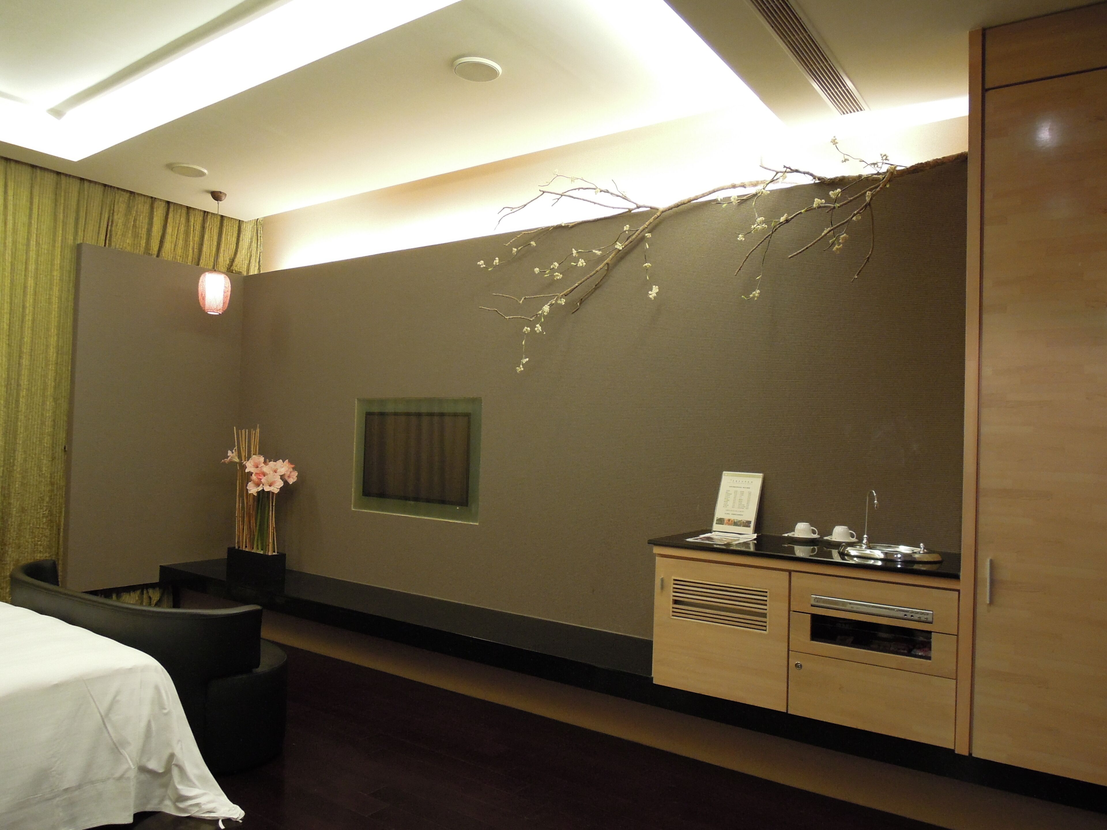 A hotel room with a bed, a small seating area, a vanity with a mirror, and a wall-mounted shelf.
