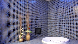 Un baño con una bañera grande, mosaicos azules y dos jarrones con flores.