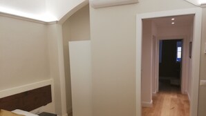 Hotellihuone, jossa on sänky, vaatekaappi, ilmastointilaite ja käytävä, joka johtaa toiseen huoneeseen.