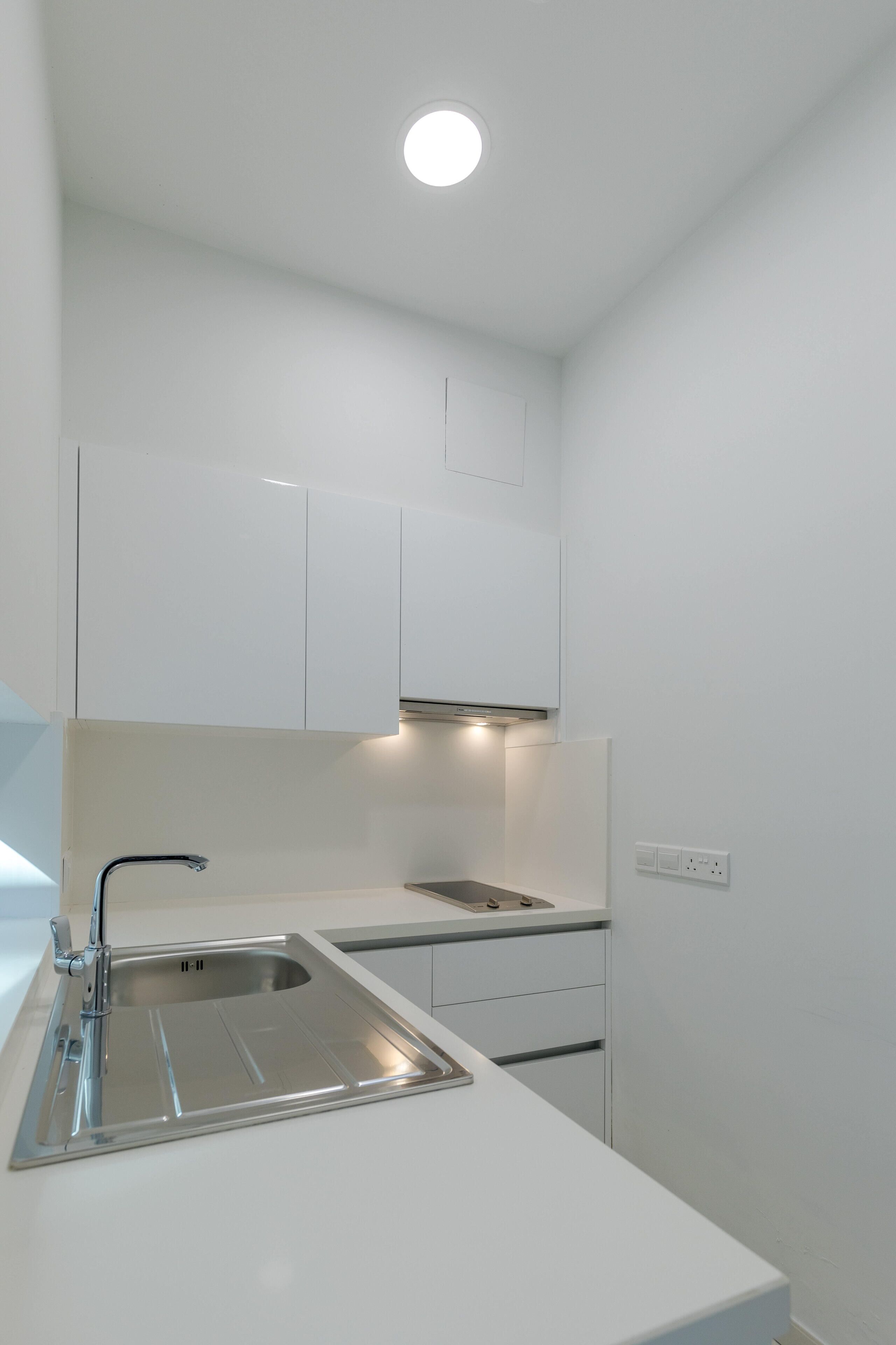 Une cuisine moderne avec des meubles blancs, un évier en acier inoxydable et un luminaire encastré au plafond.
