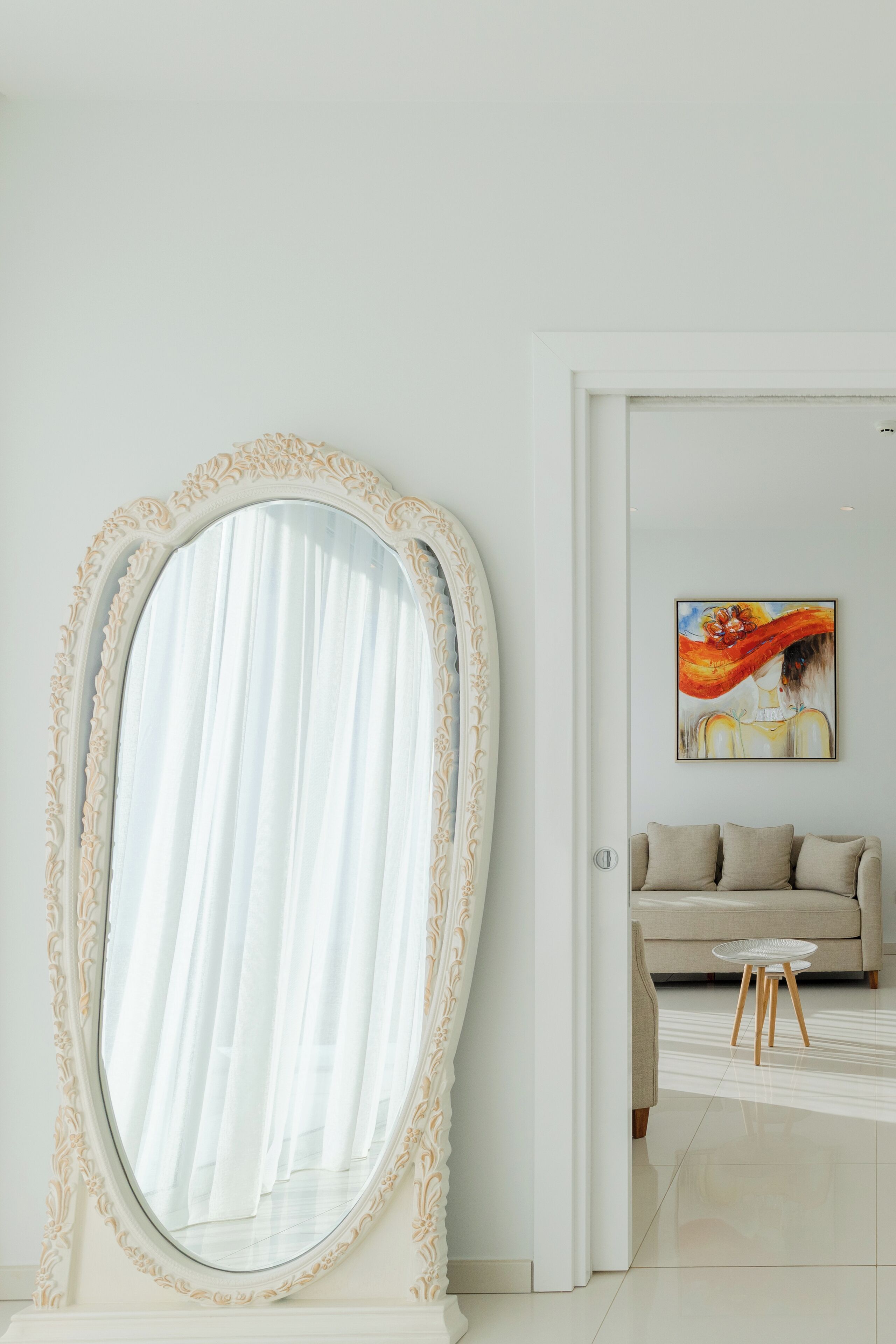 Una habitación con un espejo grande y ornamentado, un sofá color beige y una pequeña mesa redonda.