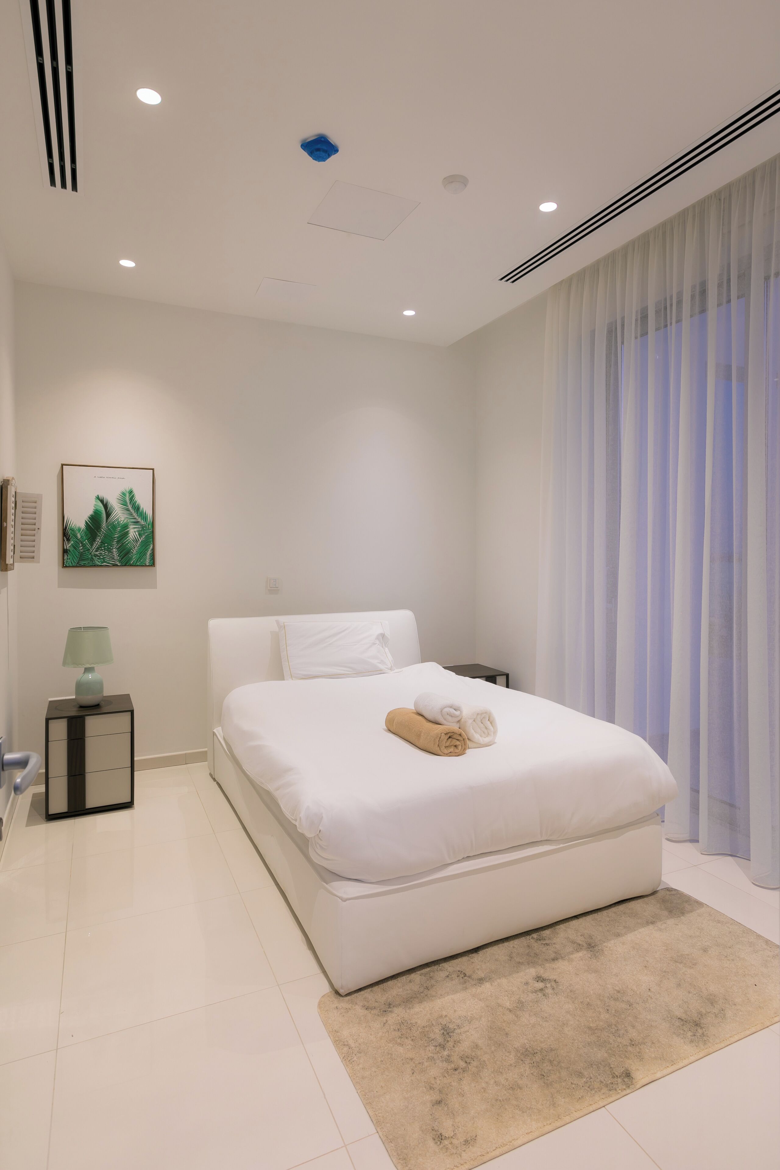 A modern bedroom with a large bed, a bedside table, a lamp, and a window with curtains.