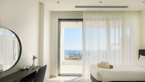 A hotel room with a bed, a desk, a chair, a large mirror, and a view of the ocean. - Sea Pearl Beachfront Villas (Ayia Napa)