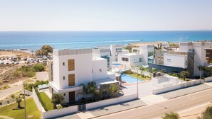 A modern resort with multiple white buildings, a swimming pool, and a view of the ocean. - Sea Pearl Beachfront Villas (Ayia Napa)
