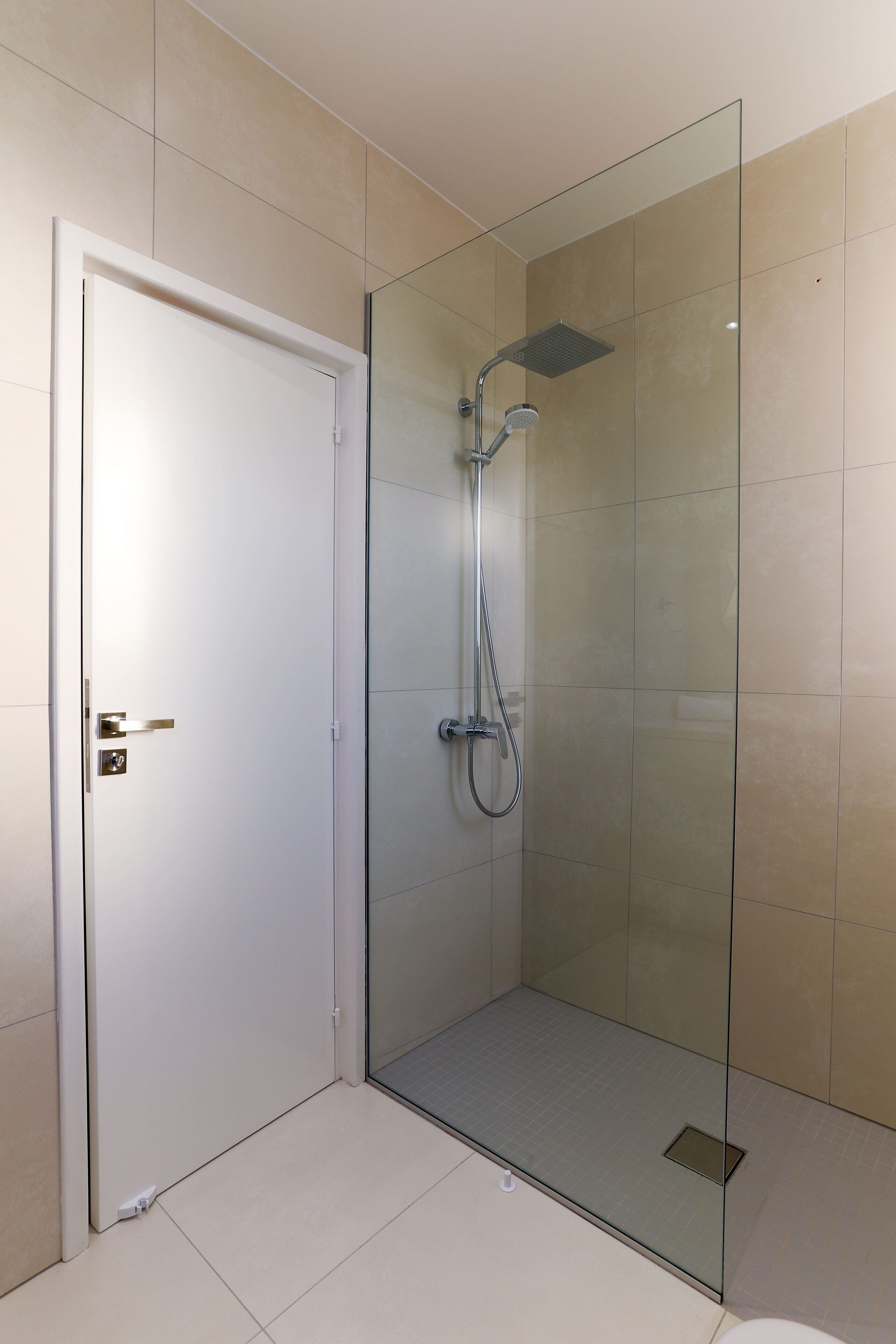 Un baño moderno con ducha acristalada, una puerta blanca y suelo de baldosas.