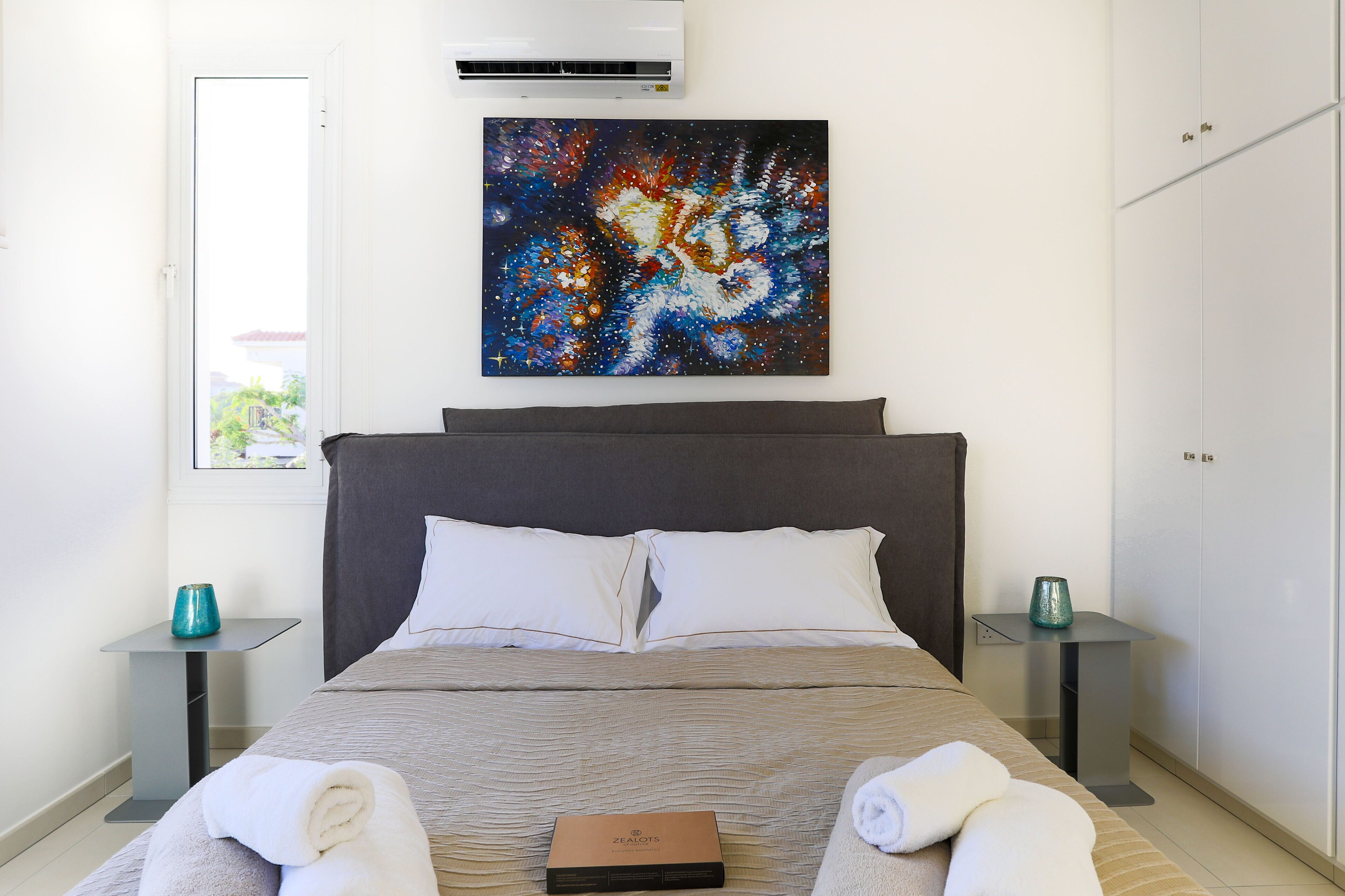 Una habitación de hotel con cama, un cuadro en la pared, una ventana y un armario.