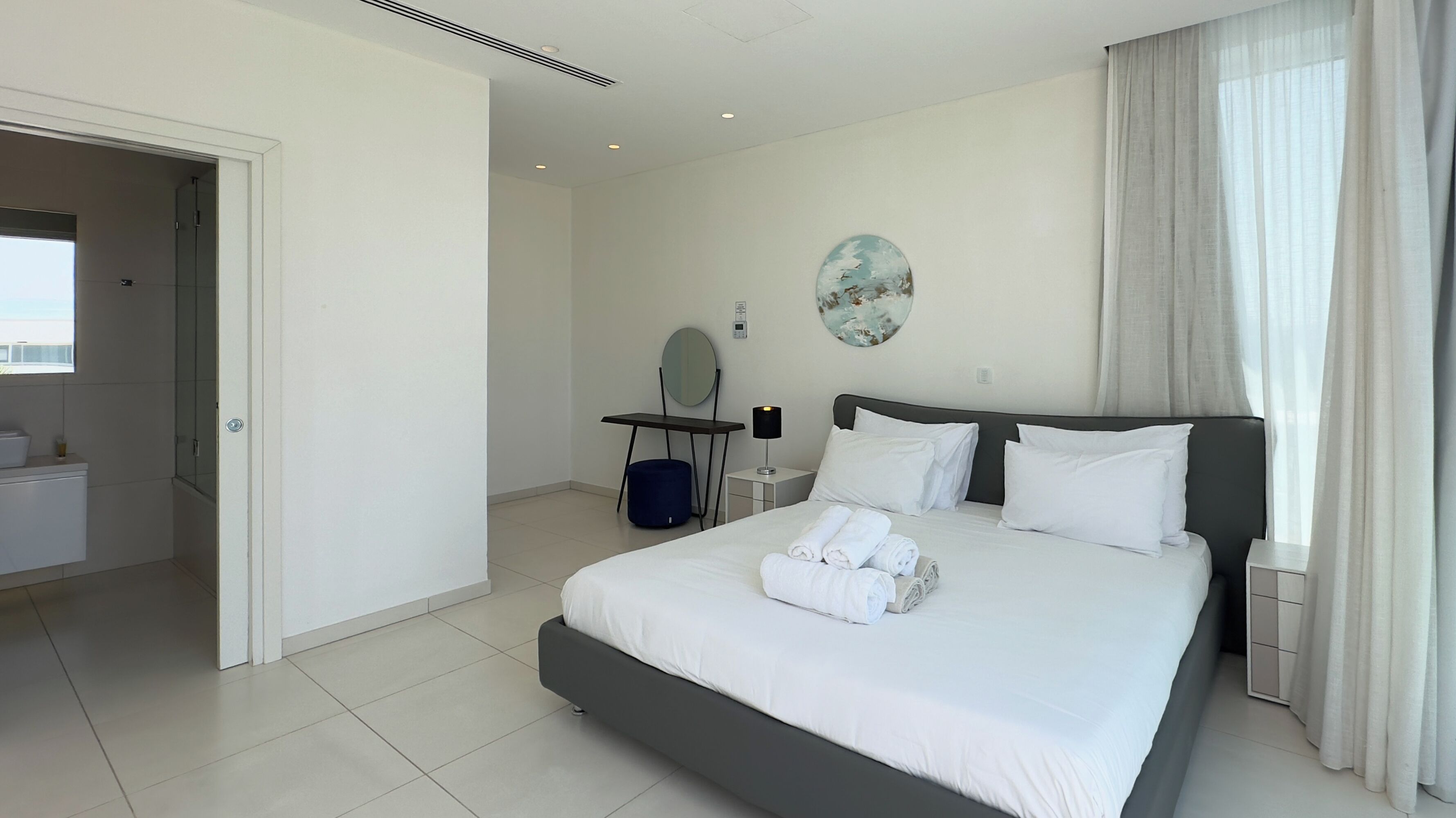 A modern hotel room with a large bed, a desk, a chair, a mirror, and a view of the outdoors.