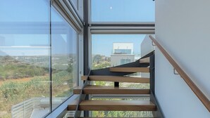 Una scala moderna con ringhiere in vetro e gradini in legno che conduce a un balcone con vista sulla città.