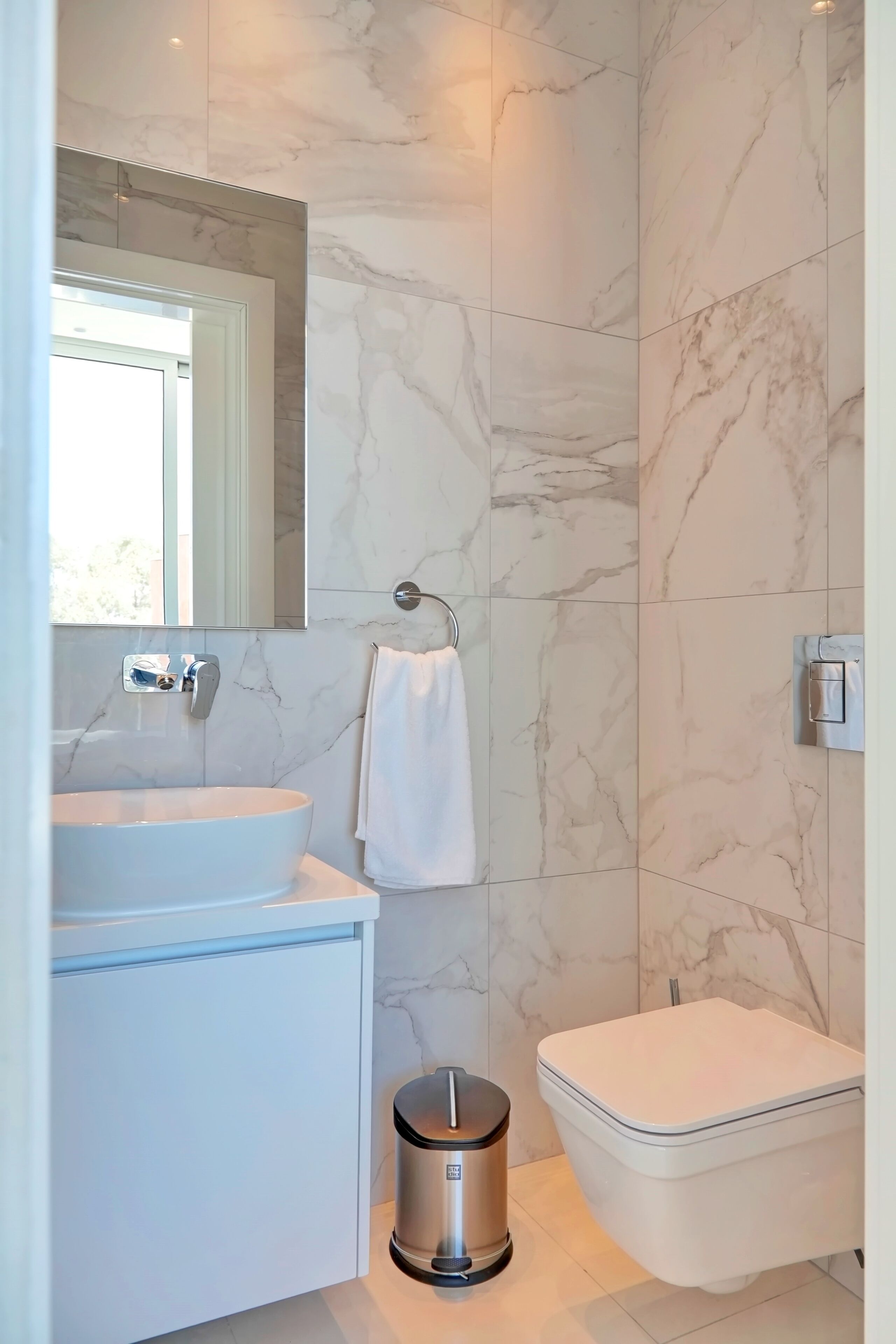 Ein modernes Badezimmer mit Marmorwand, Waschbecken, Toilette und Mülleimer.