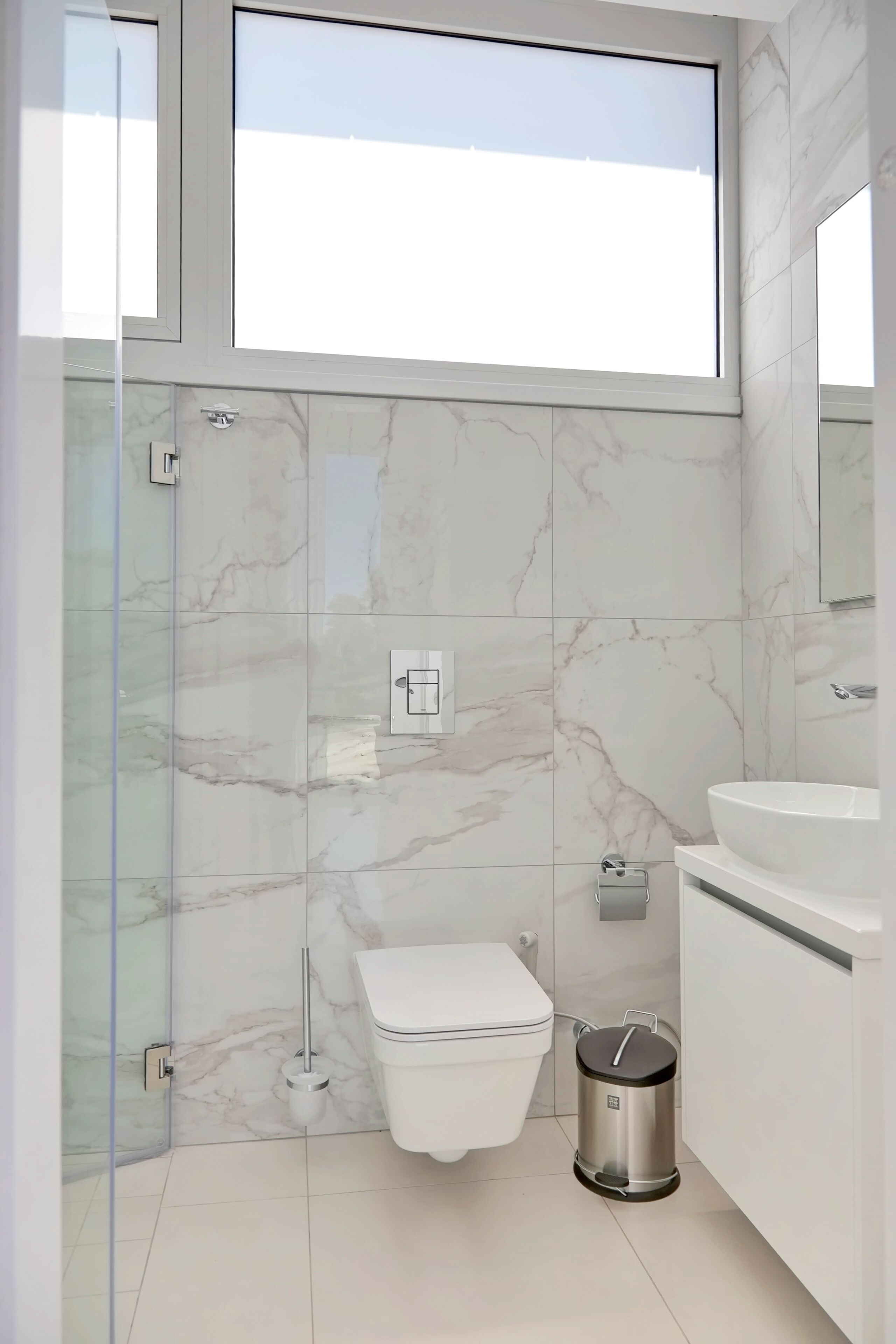 Une salle de bain moderne avec une douche à parois de verre, des toilettes, un lavabo et une poubelle.