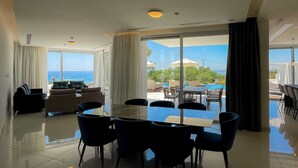 A spacious room with a large dining table and chairs, a sofa set, and a view of the ocean through large windows.