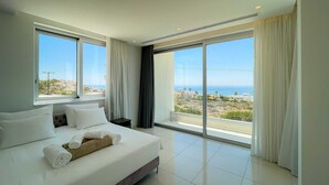 A modern hotel room with a large bed, two windows with curtains, and a view of the coastline.