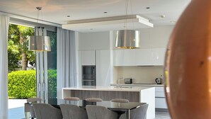 Una cocina moderna con una isla central, electrodomésticos de acero inoxidable y un área de comedor con sillas tapizadas en gris.
