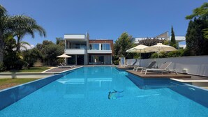 Un área de piscina moderna con una piscina rectangular, sillones de descanso y sombrillas.