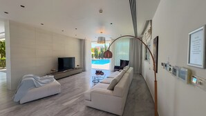 Una sala de estar moderna con un televisor grande, sofás blancos, una mesa de centro y vistas a una piscina.