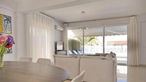 A modern living room with a dining area, large sliding glass doors leading to a pool area, and a flat-screen TV on a stand. - Μake you feel at home. Quite location deal for Family (Paralimni)