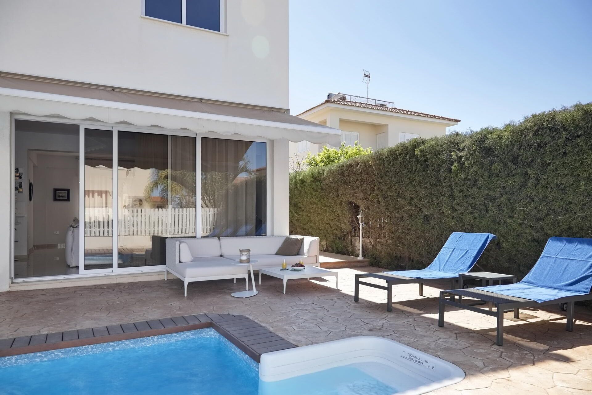 A pool area with lounge chairs, a hot tub, and a patio with a white sofa and table.