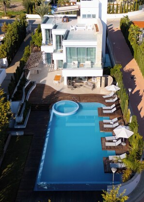Vista aérea de un hotel moderno con piscina, tumbonas y un patio.