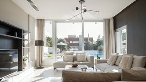 En moderne stue med sofa, fjernsyn og udsigt til en swimmingpool.