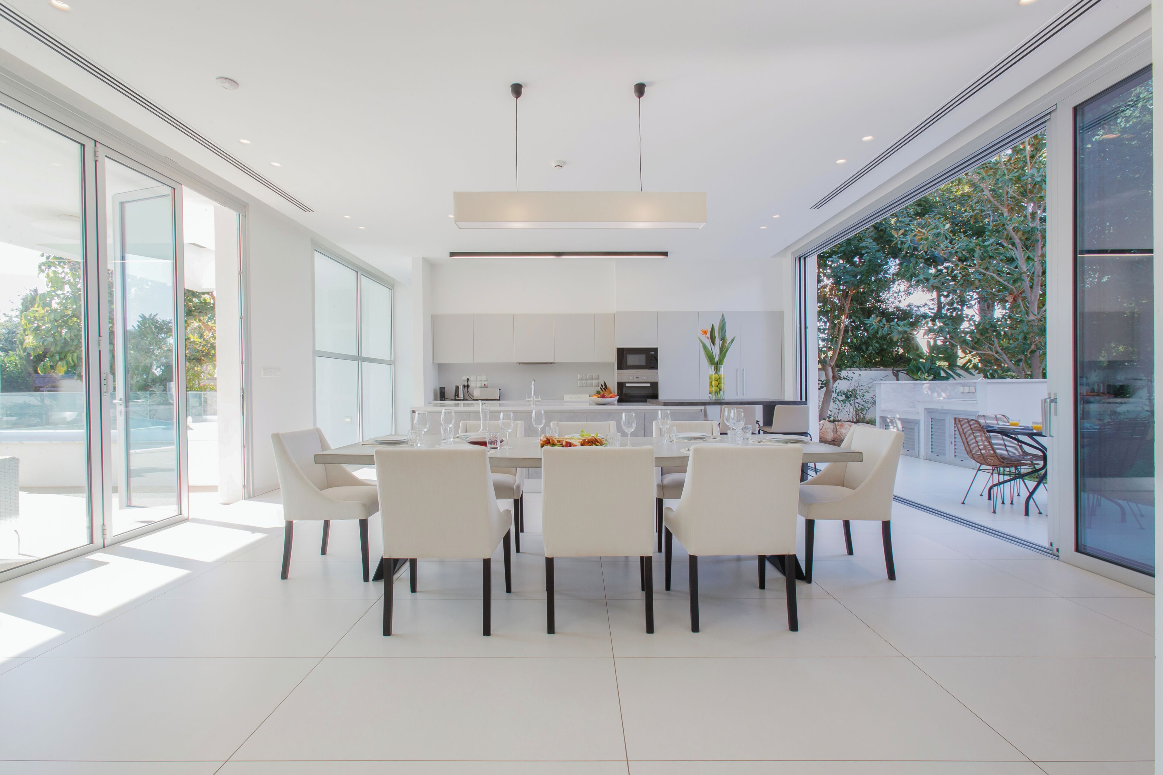 A modern kitchen with white cabinets, a central island, and a dining area with white chairs and a table.