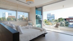 Et moderne soveværelse med en stor seng, en balkon med udendørs møbler og udsigt over byen.