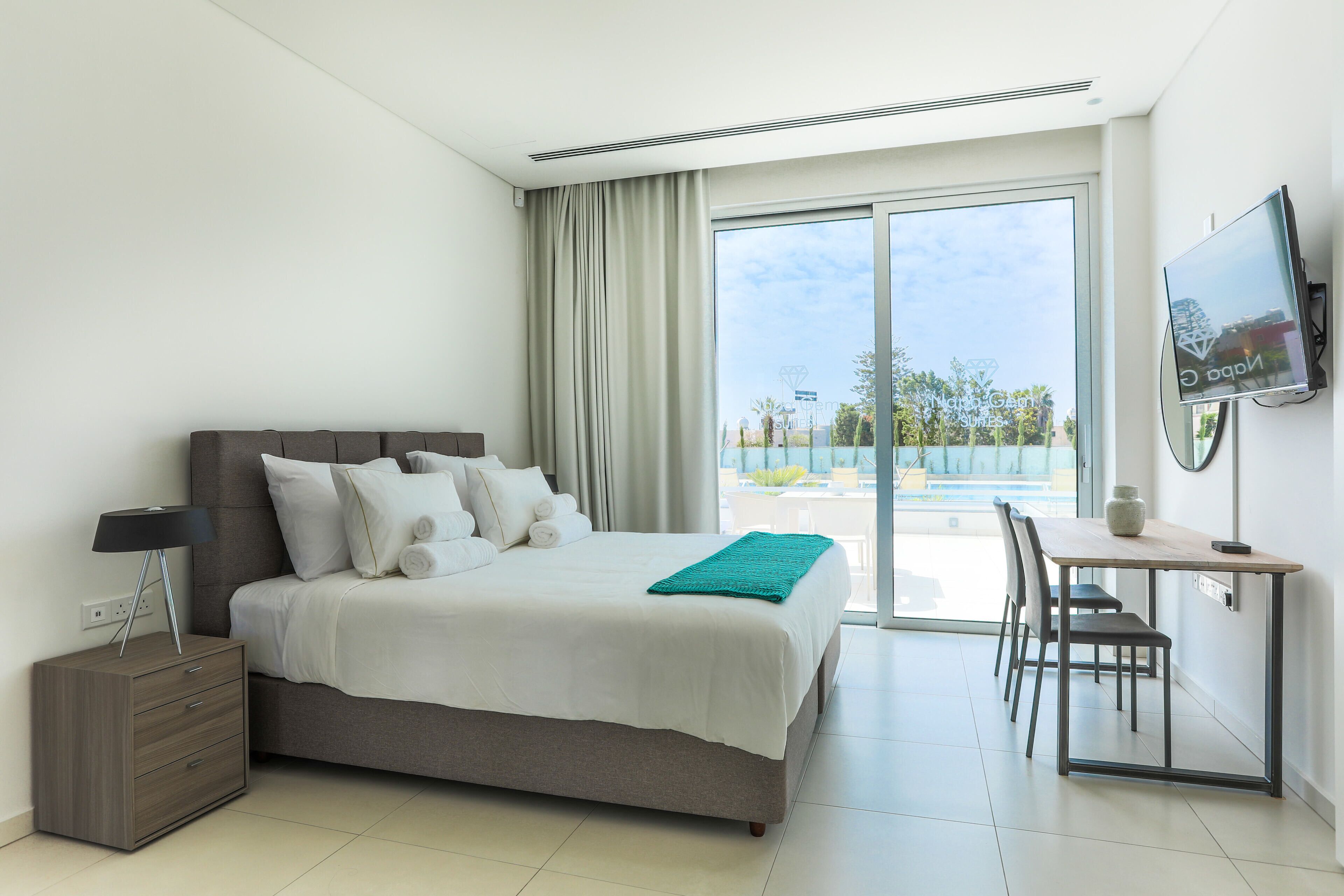 Quarto de hotel moderno com uma cama grande, uma escrivaninha e uma televisão.