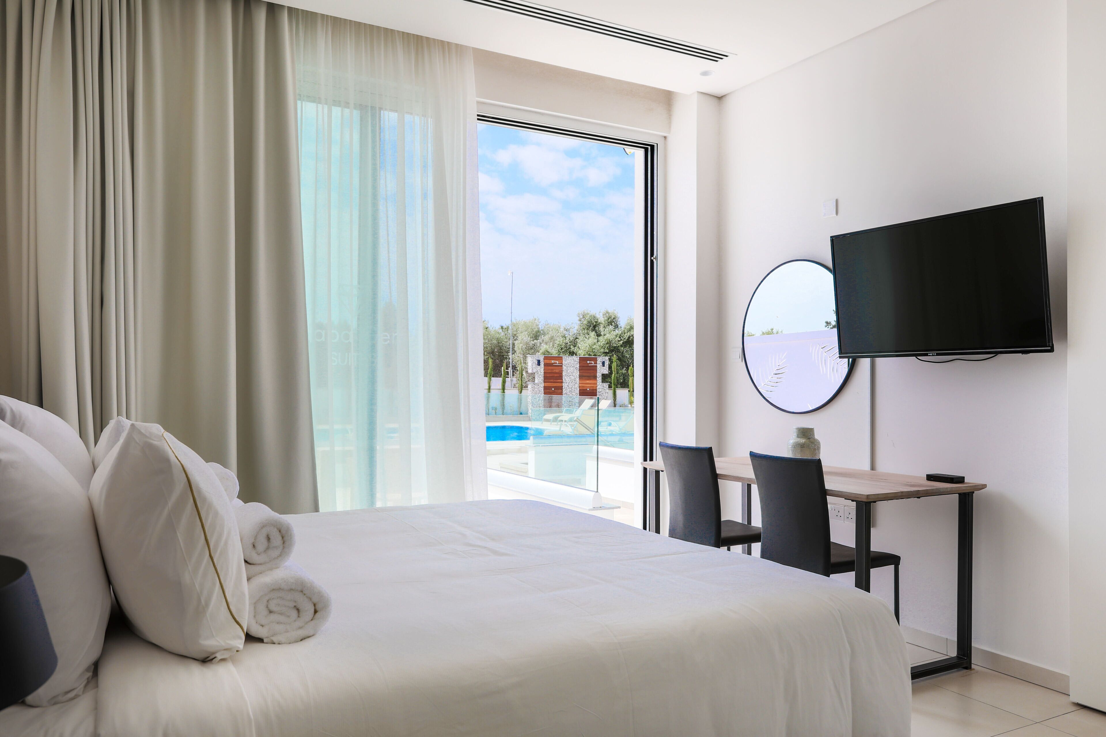 A hotel room with a large bed, a desk with a chair, a TV, and a view of a swimming pool.