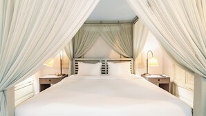 Ein großes Bett mit weißen Leinentüchern, zwei Nachttische mit Lampen und durchscheinende Vorhänge, die das Bett umrahmen.