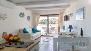 Ein modernes Wohnzimmer mit Sofa, Esstisch und Stühlen. Durch eine Schiebetür bietet sich ein Blick ins Freie.