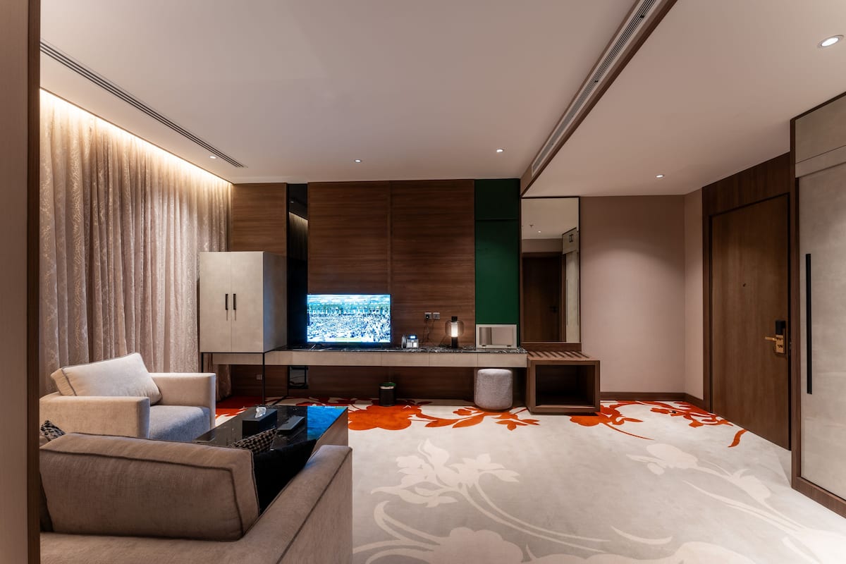A modern hotel room with a large flat-screen TV, a sofa, a coffee table, and a decorative carpet.