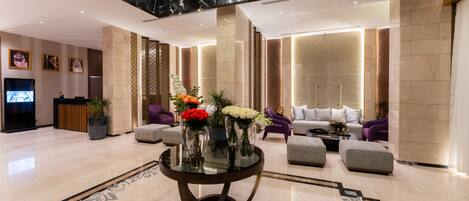 Un moderno vestíbulo con piso de mármol, una mesa de vidrio central con flores y una zona de estar con sofás.