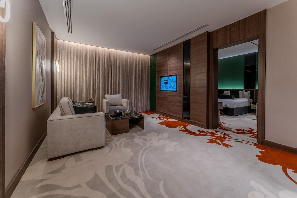 A modern hotel room with a sofa, armchair, and a flat-screen TV mounted on the wall.