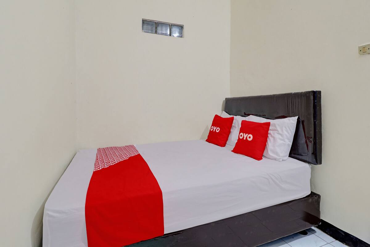 Ein Bett mit weißer und roter Bettdecke, zwei rote Kissen mit dem Aufdruck "OYO" und ein dunkles Kopfstück.