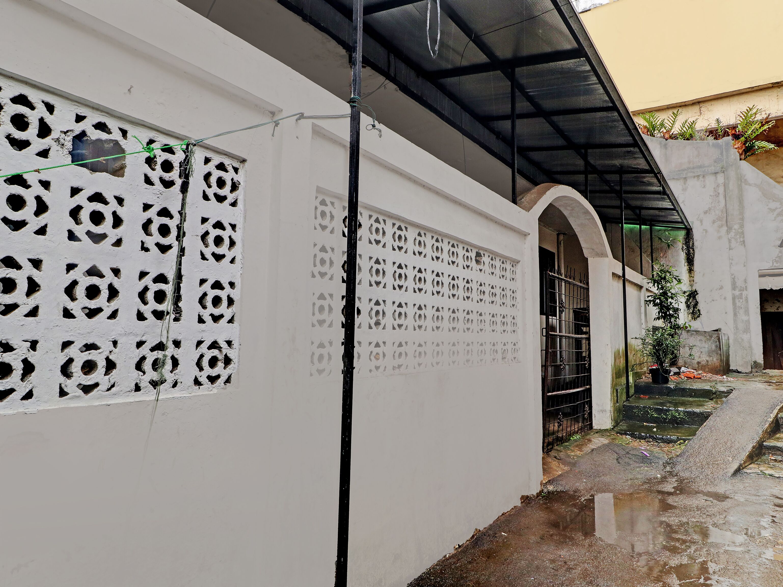 A white building with decorative cutouts on the walls, a metal gate, and a concrete staircase leading to a covered area.