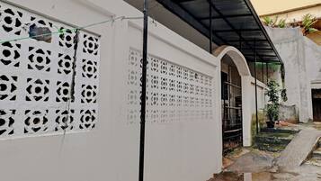 A white building with decorative cutouts on the walls, a metal gate, and a concrete staircase leading to a covered area.