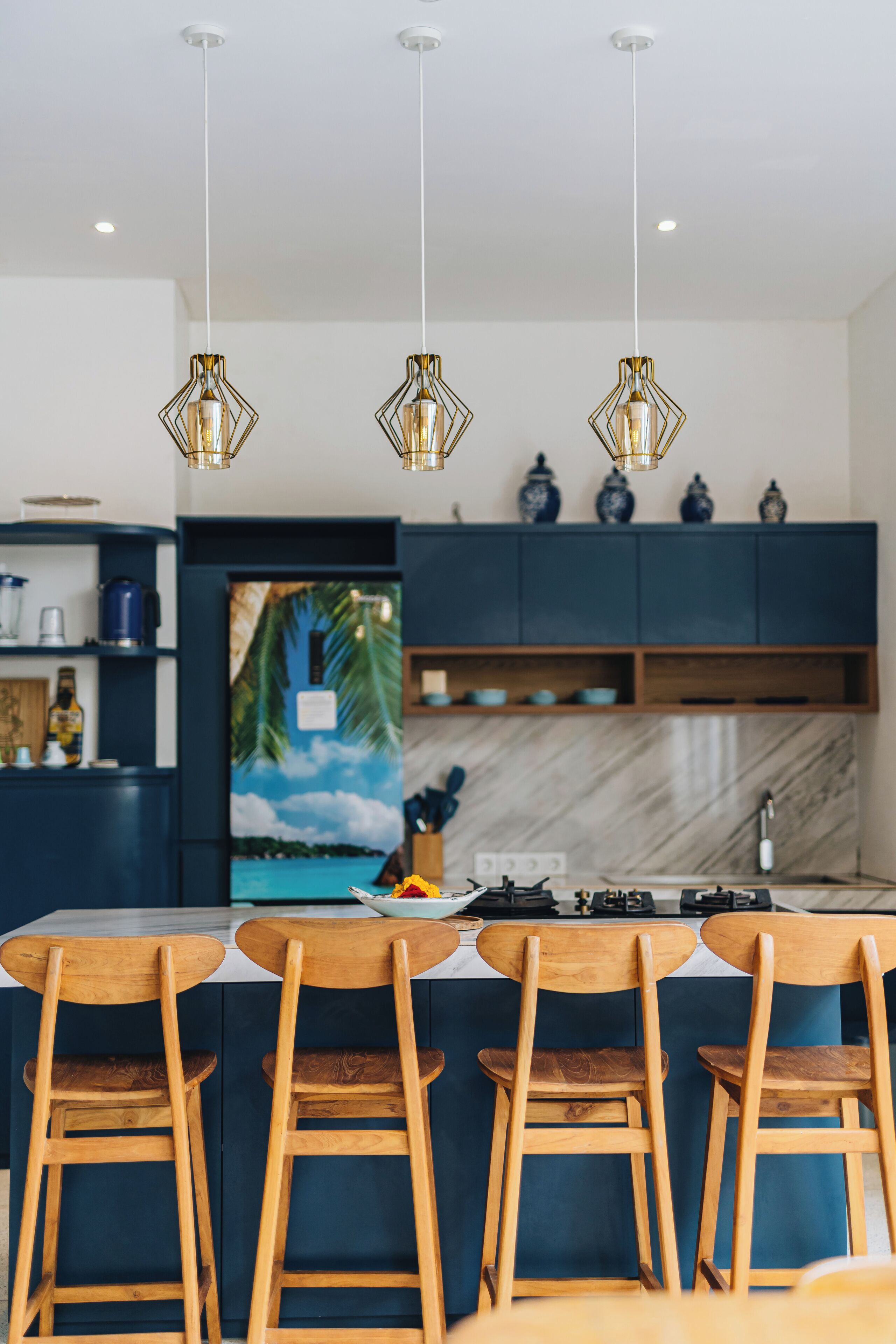 A modern kitchen with dark blue cabinets, a central island with bar stools, and pendant lighting.