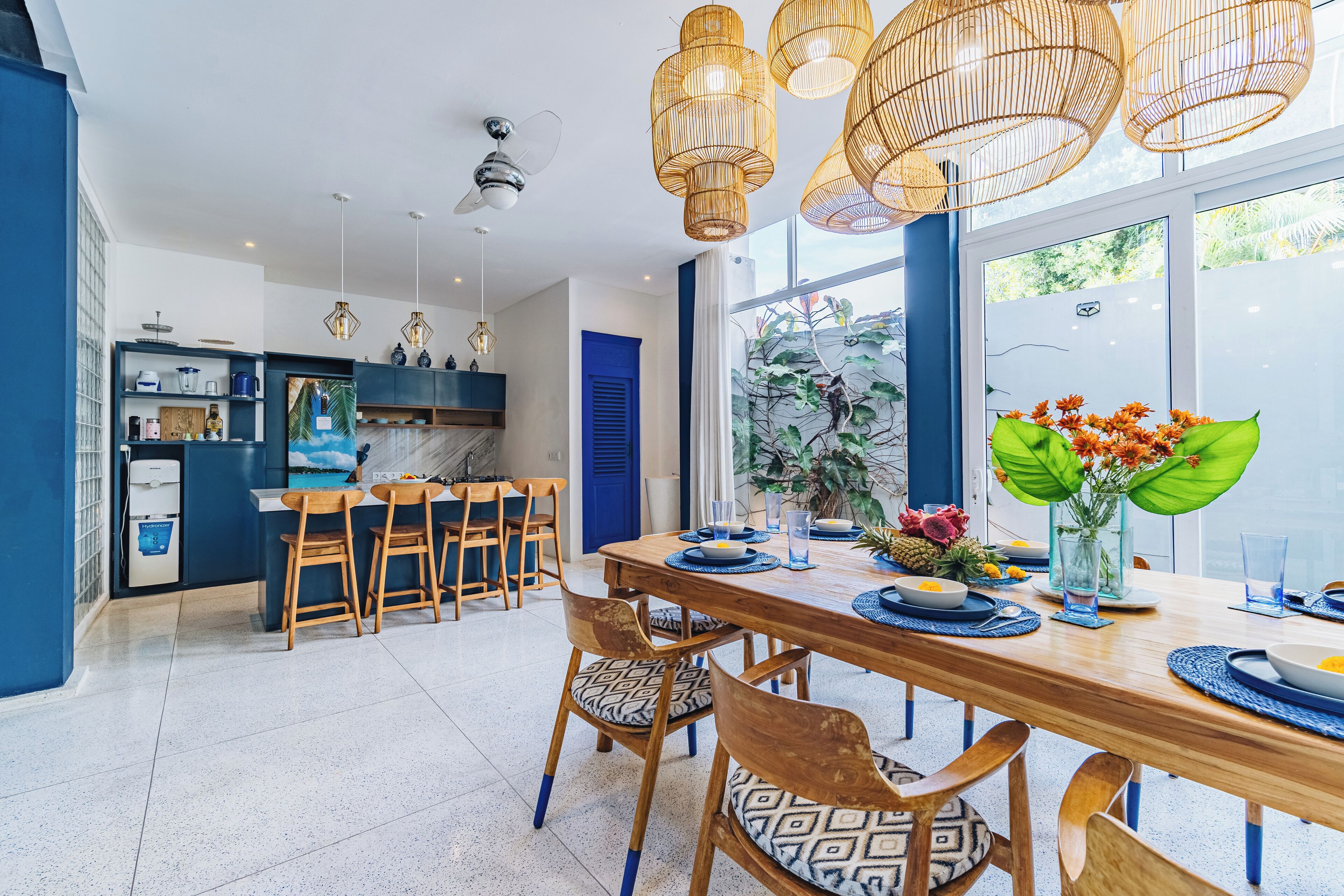 A modern kitchen with a blue door, wooden chairs, and a dining table set for six.