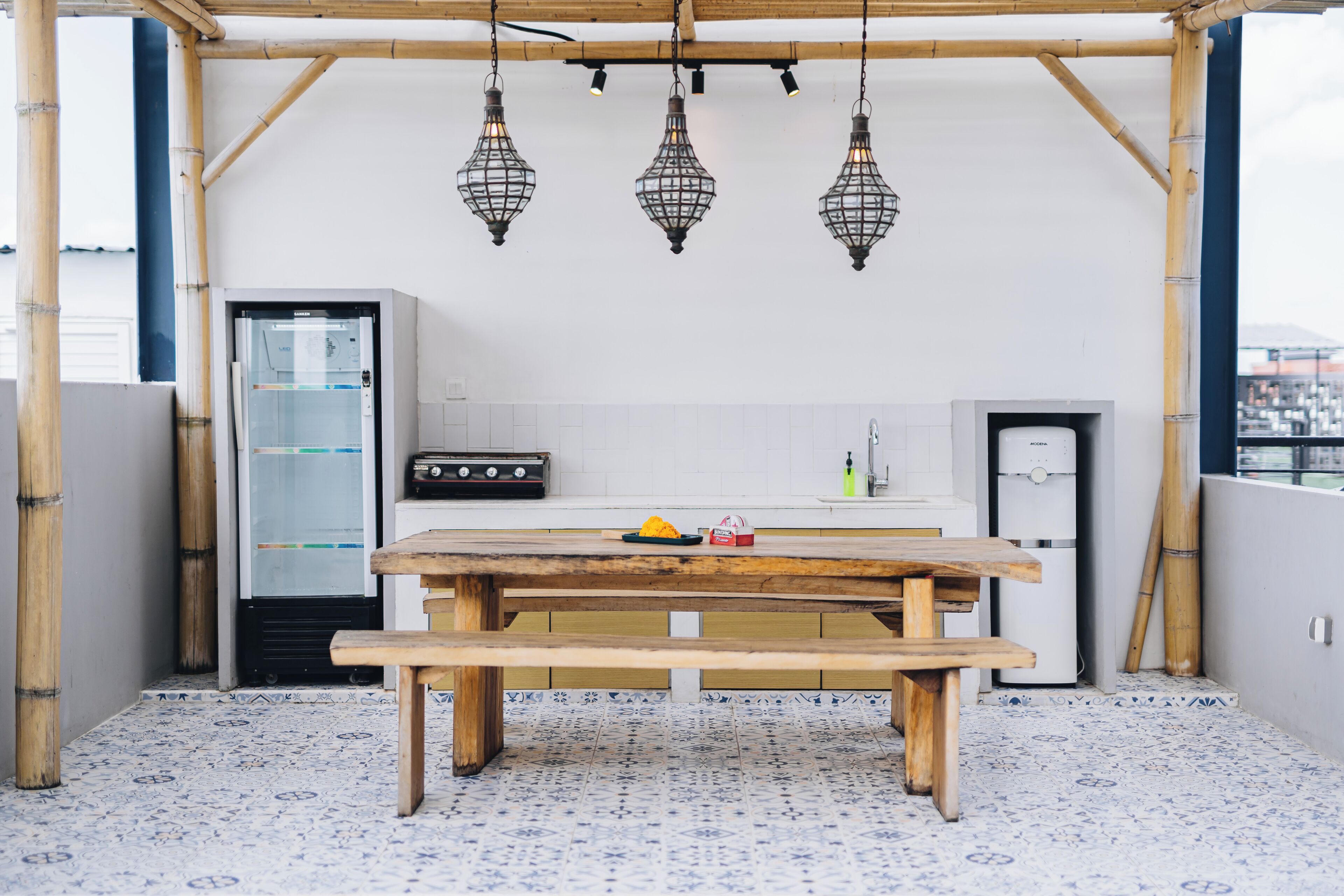 Une cuisine avec une table en bois, des luminaires suspendus et un réfrigérateur.