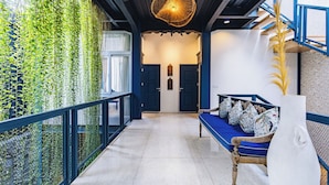 Un couloir avec un banc bleu, un vase blanc et un luminaire suspendu.