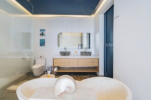 Een moderne badkamer met een vrijstaand bad, een toilet en een wastafel met spiegel.
