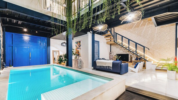 Une piscine intérieure avec une porte bleue, un escalier et un coin salon équipé d’un téléviseur.