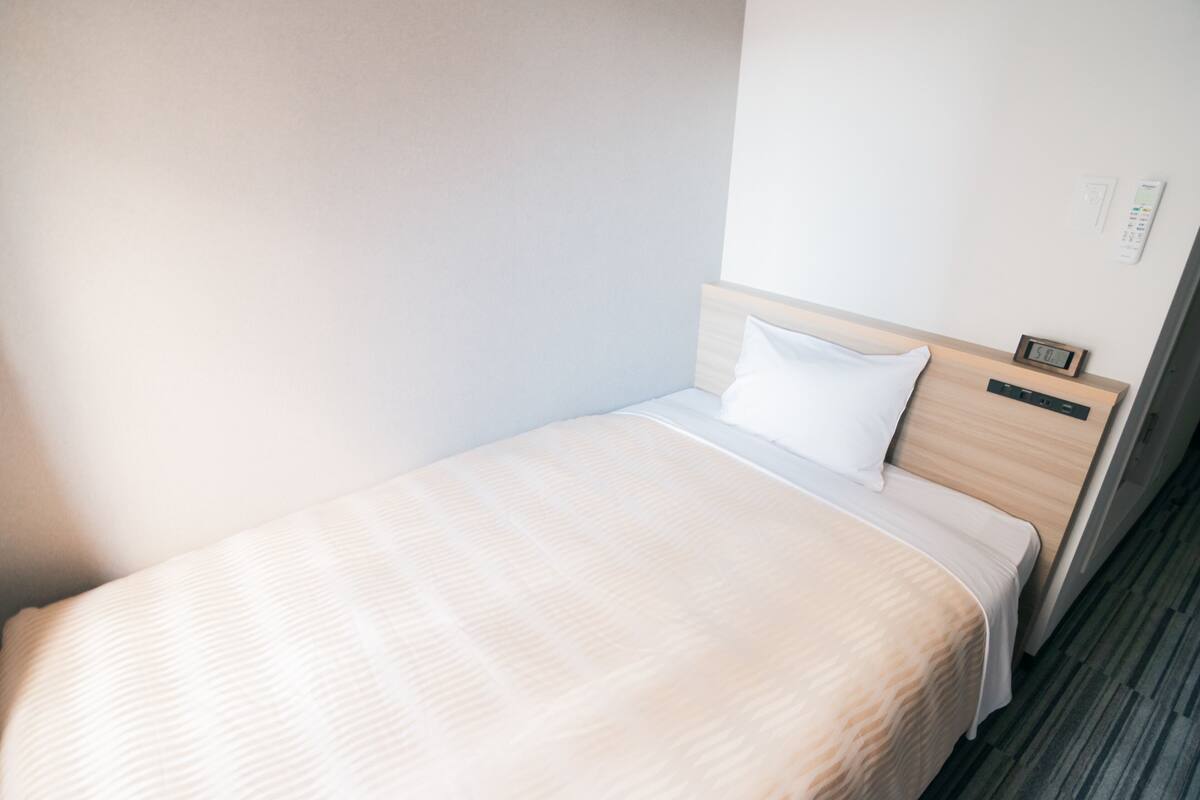 A single bed with a wooden headboard, white bedding, and a small bedside table with a clock.