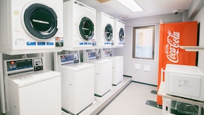 A laundry facility with multiple washing machines and dryers, a Coca-Cola vending machine, and a window providing natural light. -  Quintessa Hotel Chiba Funabashi (Funabashi)
