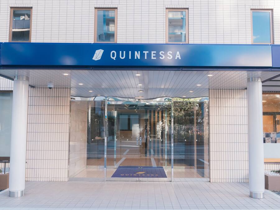 A modern hotel entrance with a clear glass door, a blue sign reading "QUINTESSA", and a tiled floor.