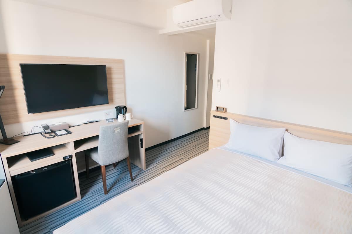 A hotel room with a bed, a desk with a computer, a chair, and a flat-screen TV.
