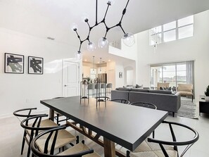 A modern dining area with a long table, chairs, and a unique chandelier. - Theme Park Villa: Pool, Game Room, Family Getaway! (Davenport)