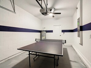 A room with a ping pong table, a ceiling fan, and a door.