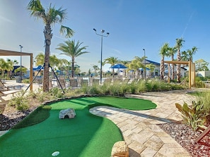 A landscaped outdoor area with a putting green, palm trees, and lounge chairs.