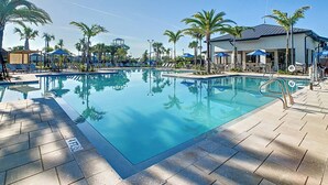 A swimming pool with lounge chairs and umbrellas, surrounded by palm trees and a building with a covered patio.