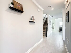 A hallway with a staircase, a framed picture on the wall, and a plant on a shelf. - Theme Park Villa: Pool, Game Room, Family Getaway! (Davenport)